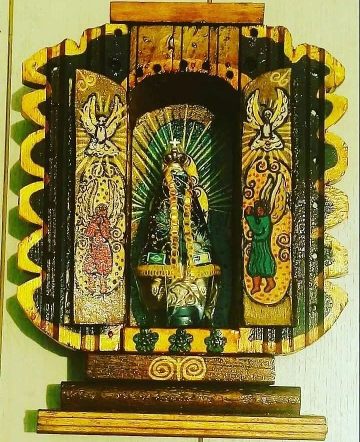 Open black and yellow oratório with a cut-out outline, with Our Lady of Aparecida among green rays and angels on the doors