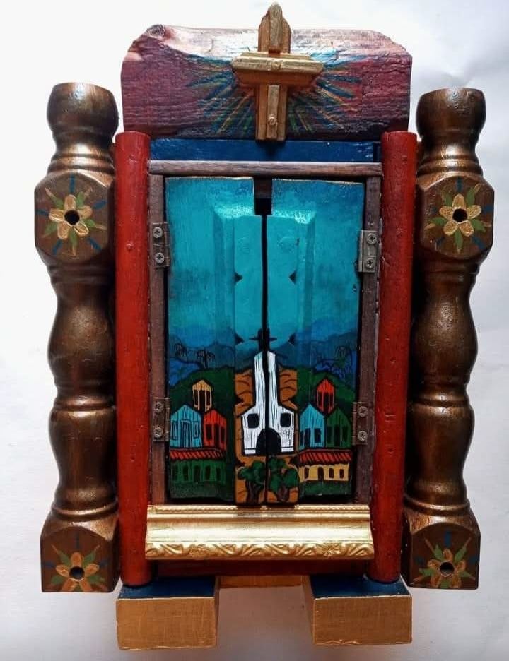 Closed oratório between two columns and red pillars, with a white church and houses under a turquoise sky on the doors